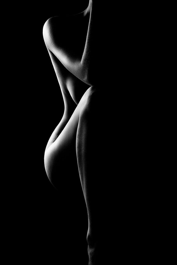 A black and white photo of a nude human figure posed sideways, with dramatic lighting creating deep shadows and highlighting the curves—evoking the tranquil artistry found in Brisbane massage studios or among private masseurs.