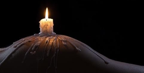 A lit candle sits on a curved surface, with melted wax dripping down. The dark background highlights the candle's warm glow—perfect for setting a tranquil mood during a relaxing Brisbane massage session.